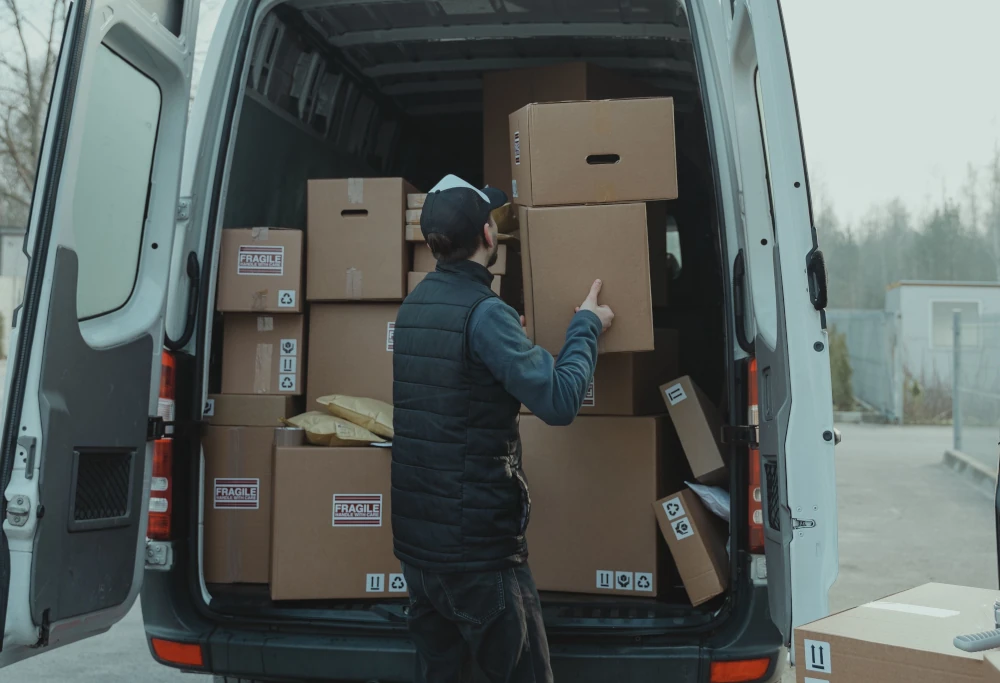 Delivery courier arranging fragile cardboard packages inside the back of a fully loaded white cargo van.